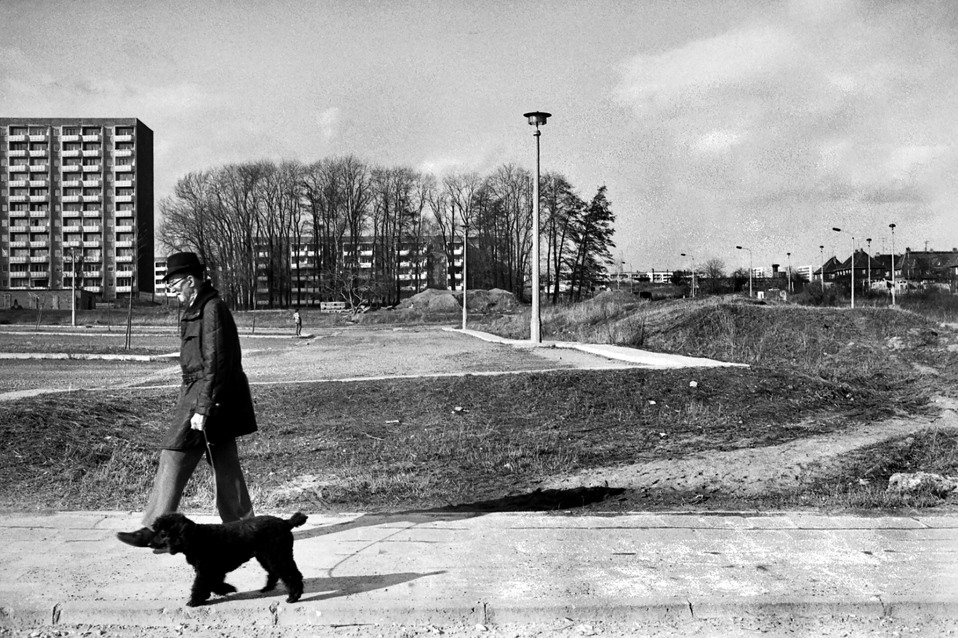Ein älterer Mann geht mit seinem Hund spazieren. Im Hintergrund zu sehen sind die Plattenbauten in Weimar-West, ein Sandberg lässt auf Baustelle für weitere Wohnhäuser schließen.